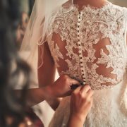 Bridesmaid helping bride fasten corset close-up and getting her dress, preparation concept in morning for wedding ceremony.